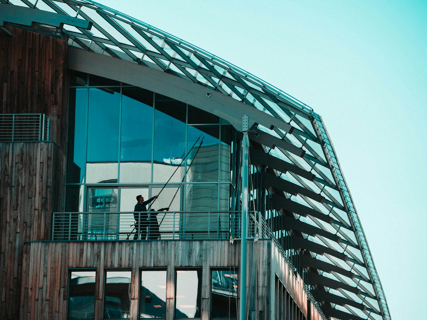 A window cleaner uses a long pole on a modern building.