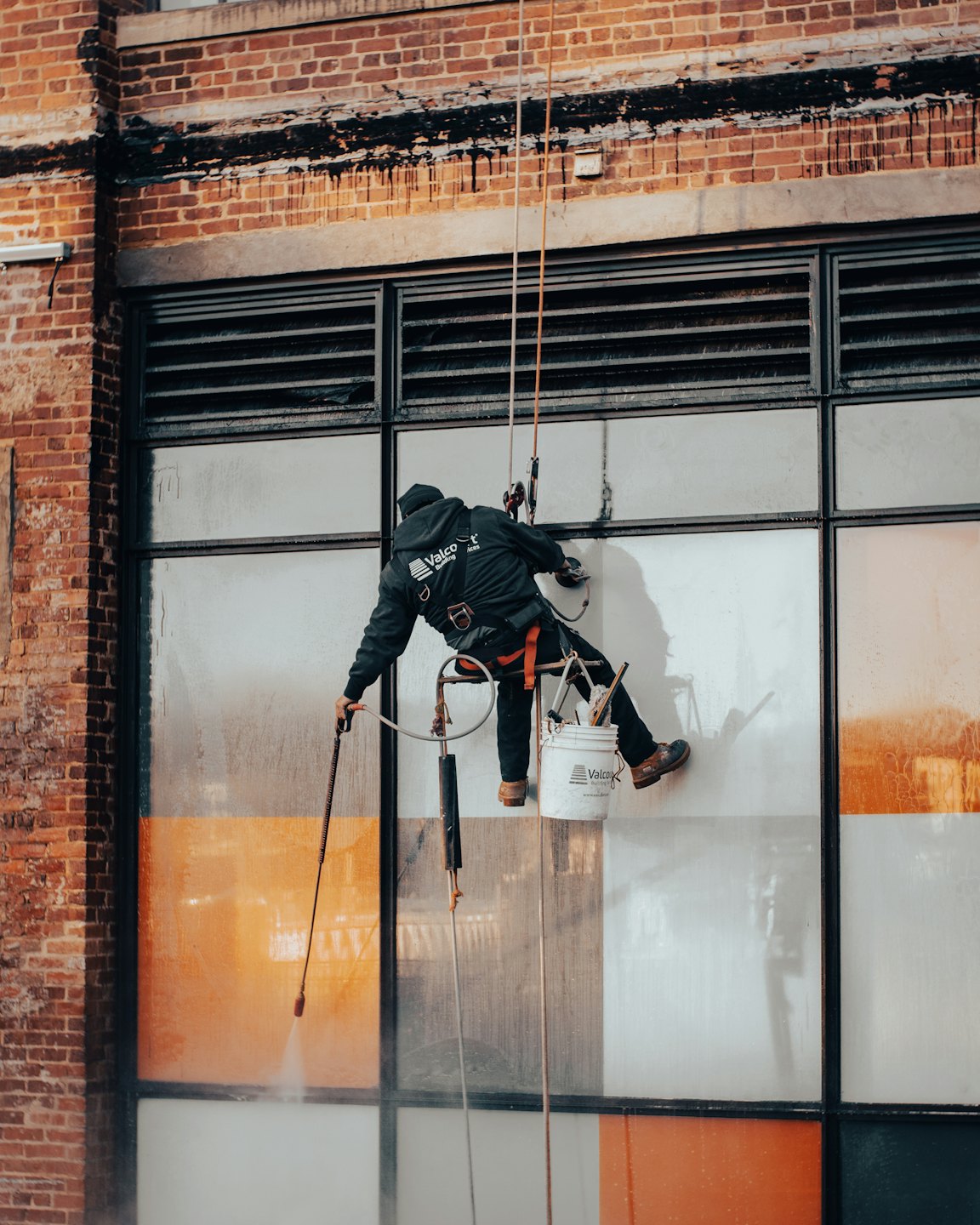 Window cleaner rappels down brick building power washing windows.