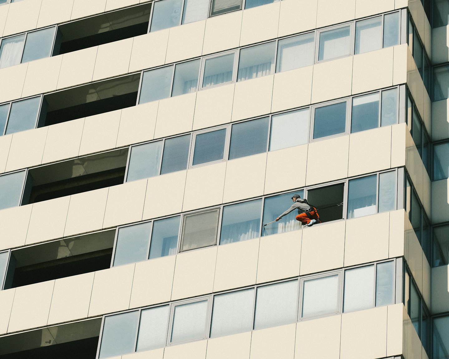 Window cleaner in orange trousers on high-rise ledge.